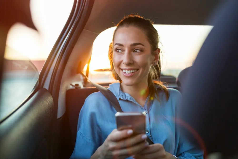 Smiling passenger relaxing in the back of a chauffeur-driven car at golden hour on a day trip from London