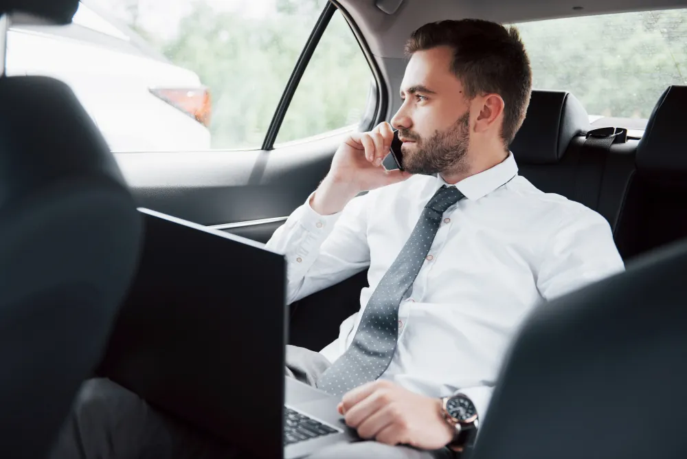 Businessman working on a laptop and phone in the back of an executive chauffeur-driven car on the way to a corporate event in London