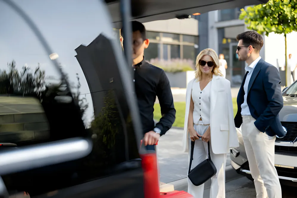 Chauffeur loading luggage for two smartly dressed travellers arriving for a Heathrow airport transfer